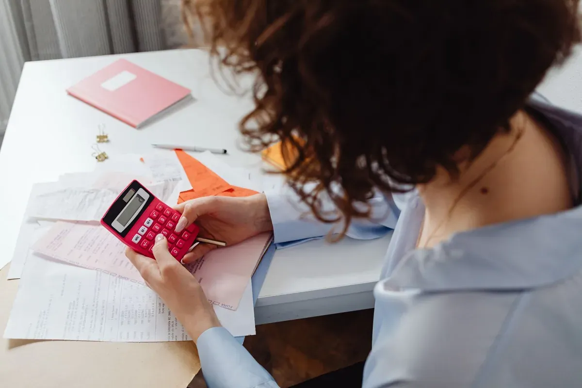 Woman calculating monthly budget with notepad and calculator after 401k match was paused