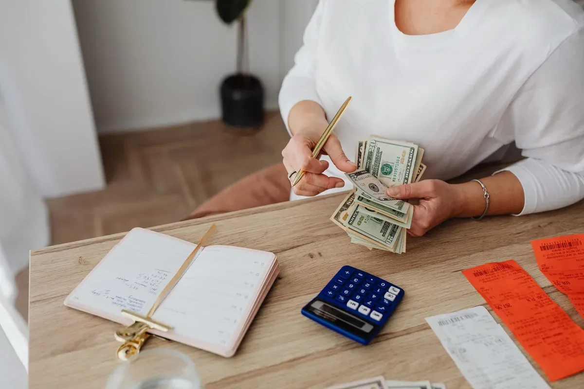 A person calculating bills at a kitchen table with a notebook and calculator