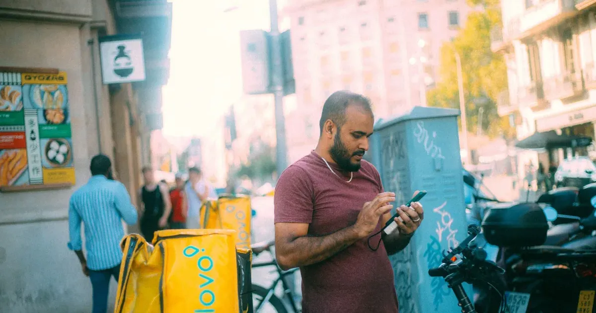 Man checking his phone on a city street while reviewing hidden bank fees on his checking account