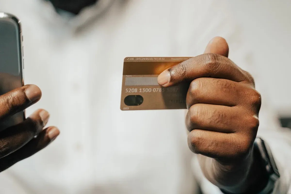 Close-up of a hand holding a credit card and smartphone, representing digital moneymaxxing habits like rewards tracking