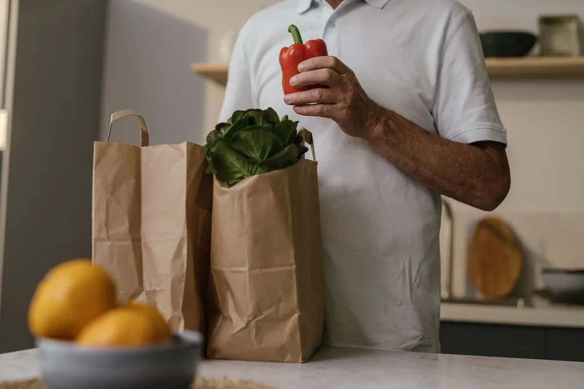 Person holding a red bell pepper next to grocery bags on a kitchen counter, representing cashback tracked on grocery spending