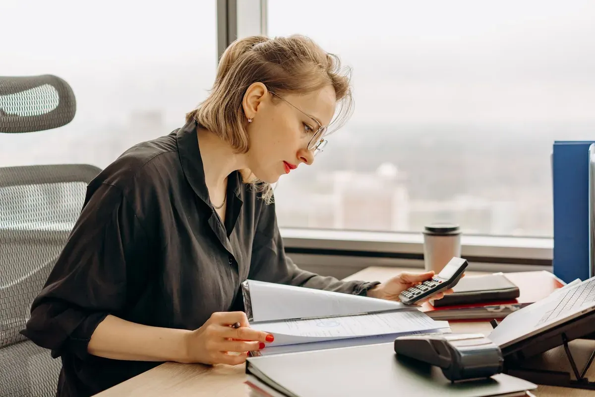 Woman reviewing paperwork with a calculator at a desk, tracking the impact of the 2027 Social Security COLA on her budget