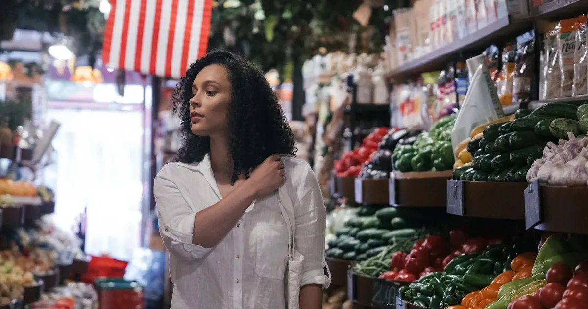 Woman shopping in a fresh produce market aisle — tracking grocery budget against 2026 tariffs